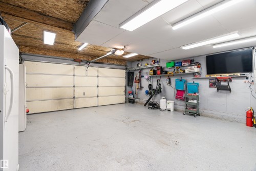 The property offers a garage with a roll-up door, exposed wood ceiling, and fluorescent lighting - 442 Hunters Green, Edmonton, AB - Indoor Photo Showing Garage