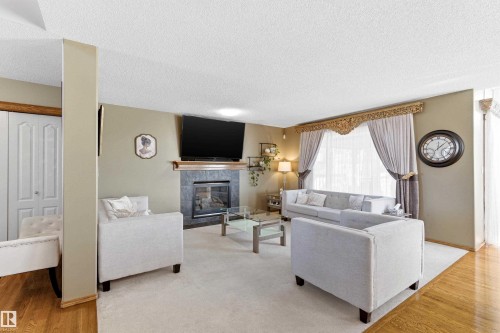 This inviting living area features a fireplace with a stone surround, hardwood floors, and a large window with ornate valance - 442 Hunters Green, Edmonton, AB - Indoor Photo Showing Living Room With Fireplace