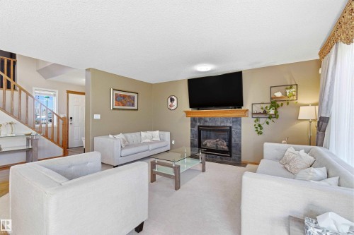 The living room features a fireplace with a stone tile surround and a wooden mantel, a large window with drapes, and carpeted flooring - 442 Hunters Green, Edmonton, AB - Indoor Photo Showing Living Room With Fireplace