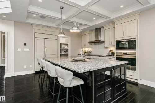 The kitchen features a large island with a light-colored granite countertop, dark cabinetry, and integrated seating - 3435 Keswick Boulevard, Edmonton, AB 