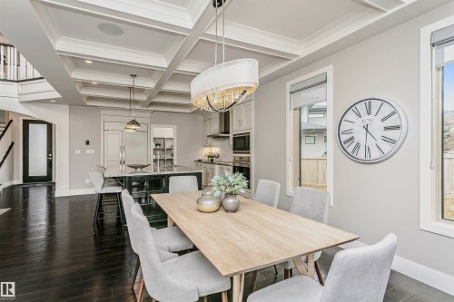 This expansive open-concept living space features dark hardwood flooring, a coffered ceiling, and a dining area with large windows providing natural light - 3435 Keswick Boulevard, Edmonton, AB 
