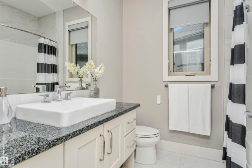 Bathroom featuring a vanity with a rectangular basin sink and granite countertop, a window with a roller blind, and a shower with a striped shower curtain - 3435 Keswick Boulevard, Edmonton, AB 