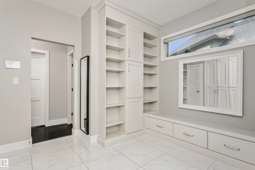 Entryway featuring white tile flooring, built-in shelving and cabinetry, and a large mirror - 3435 Keswick Boulevard, Edmonton, AB 