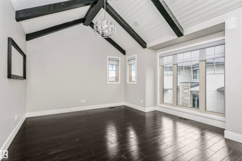 This room features dark hardwood flooring, a vaulted ceiling with exposed dark beams, and a modern light fixture - 3435 Keswick Boulevard, Edmonton, AB 
