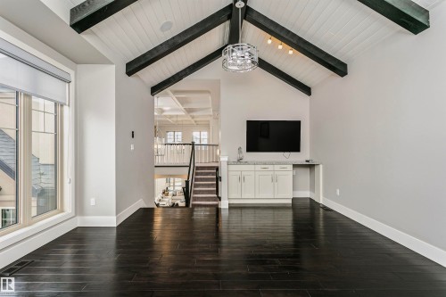 Living area featuring dark hardwood floors, a vaulted ceiling with exposed beams, a built-in wet bar with cabinetry, and large windows - 3435 Keswick Boulevard, Edmonton, AB 