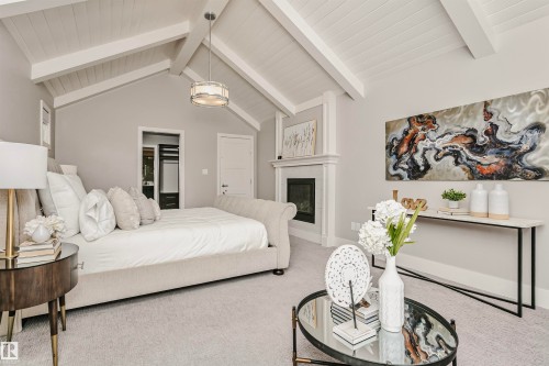 This inviting room features a vaulted ceiling with exposed beams, light-colored carpeting, and a fireplace with a decorative mantel - 3435 Keswick Boulevard, Edmonton, AB 