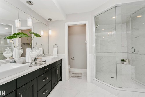 Bathroom featuring a dual vanity with white rectangular sinks, a dark wood cabinet, and a spacious glass-enclosed shower with white tiled walls - 3435 Keswick Boulevard, Edmonton, AB 