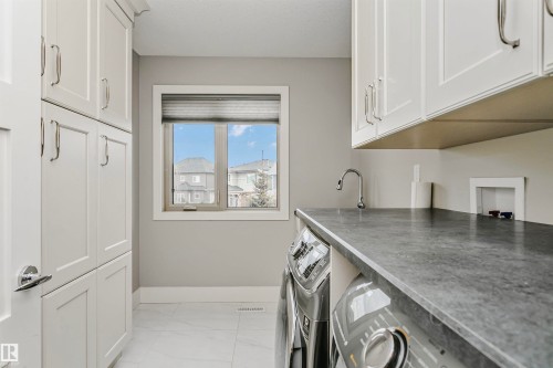 Laundry area featuring white cabinetry, a window with a blind, a countertop, and a faucet - 3435 Keswick Boulevard, Edmonton, AB 