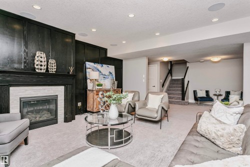 Spacious living area featuring a fireplace with a light-colored stone surround and a dark wood mantel, recessed lighting, and carpeted flooring - 3435 Keswick Boulevard, Edmonton, AB 
