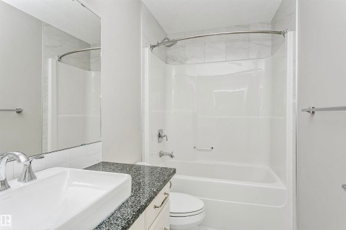 This bathroom features a vessel sink set into a dark speckled countertop, a large mirror, and a combination bathtub and shower with a curved shower curtain rod - 3435 Keswick Boulevard, Edmonton, AB 