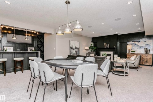 This versatile space features a wet bar with dark cabinetry, a dedicated area with a gaming table, and a living area with a fireplace - 3435 Keswick Boulevard, Edmonton, AB 