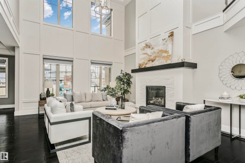The living area features high ceilings, dark hardwood floors, and a prominent white stone fireplace with a black mantle - 3435 Keswick Boulevard, Edmonton, AB 