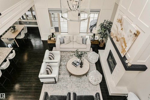 This inviting open-concept living area features dark hardwood flooring, a white brick fireplace with a dark mantle, and tall windows that provide abundant natural light - 3435 Keswick Boulevard, Edmonton, AB 