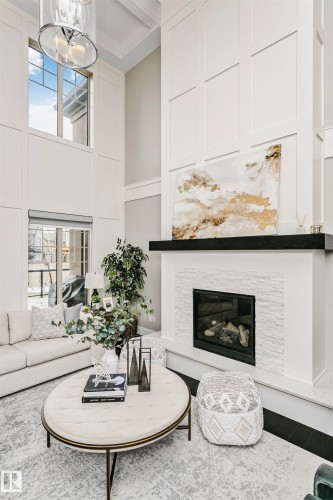 This living space features a fireplace with a stone surround and a dark mantle, complemented by high ceilings and tall windows - 3435 Keswick Boulevard, Edmonton, AB 