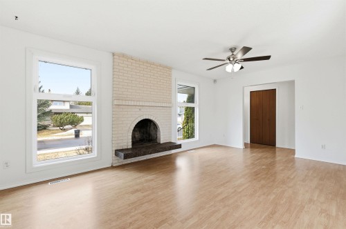 Bright living area featuring light-colored flooring, a painted brick fireplace with a dark hearth, and a ceiling fan with integrated lighting - 1707 65 Street, Edmonton, AB - Indoor Photo Showing Living Room With Fireplace