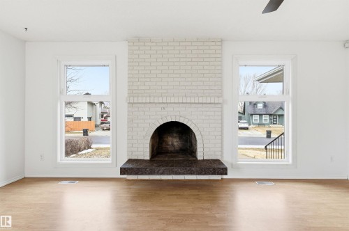 Living area featuring hardwood floors, white walls, and a white brick fireplace with a dark-colored hearth - 1707 65 Street, Edmonton, AB - Indoor Photo Showing Living Room With Fireplace