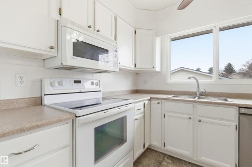 The kitchen features white cabinetry, white appliances, a double basin sink, and a large window - 1707 65 Street, Edmonton, AB - Indoor Photo Showing Kitchen With Double Sink