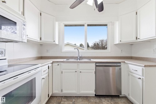 The kitchen features white cabinetry, a stainless steel dishwasher, a white oven, and a white microwave - 1707 65 Street, Edmonton, AB - Indoor Photo Showing Kitchen With Double Sink