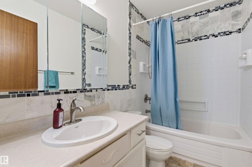 Bathroom featuring a vanity with an integrated sink, a mirrored medicine cabinet, and a bathtub with tiled surround - 1707 65 Street, Edmonton, AB - Indoor Photo Showing Bathroom