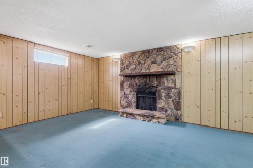 Living area featuring wood paneling on the walls, a stone fireplace with a stone hearth, and a window providing natural light - 1707 65 Street, Edmonton, AB - Indoor With Fireplace