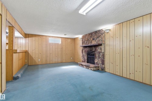 This room features wood paneling, an exposed stone fireplace, and light teal carpeting - 1707 65 Street, Edmonton, AB - Indoor Photo Showing Other Room With Fireplace