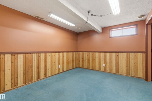 This room features light teal carpeting, wooden paneling along the lower half of the walls, and a window providing natural light - 1707 65 Street, Edmonton, AB - Indoor