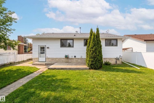 The property features a well-maintained lawn, a white exterior, and a small wooden patio area - 1707 65 Street, Edmonton, AB - Outdoor