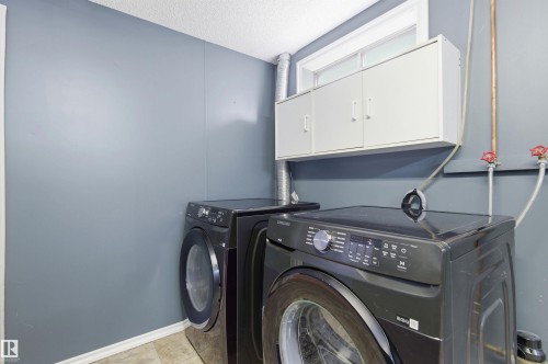 Laundry area with gray paneled walls, a window, and white overhead cabinets - 1707 65 Street, Edmonton, AB - Indoor Photo Showing Laundry Room