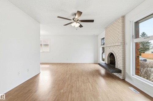 The living area features light-toned flooring, a white brick fireplace with a dark hearth, and a ceiling fan - 1707 65 Street, Edmonton, AB - Indoor With Fireplace