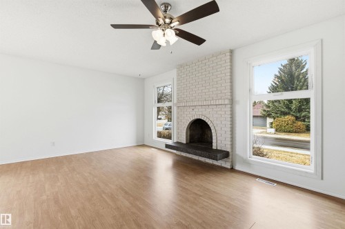 Living area with wood-look flooring, a white brick fireplace with a dark hearth, and a ceiling fan - 1707 65 Street, Edmonton, AB - Indoor With Fireplace