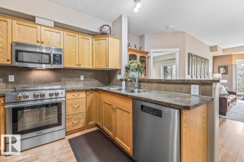 The kitchen features wooden cabinetry, a stainless steel microwave, and a stainless steel oven - 332 612 111 Street, Edmonton, AB - Indoor Photo Showing Kitchen With Double Sink