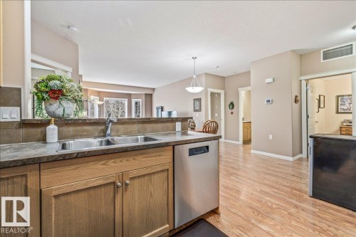 The kitchen features a double basin stainless steel sink, wood cabinetry, and a stainless steel dishwasher - 332 612 111 Street, Edmonton, AB - Indoor Photo Showing Kitchen With Double Sink