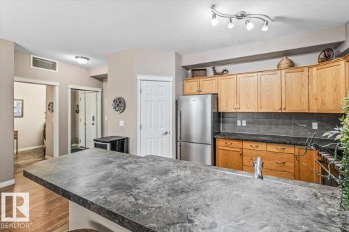 The kitchen features wood cabinetry, a stainless steel refrigerator, and a stone-look countertop with an integrated sink - 332 612 111 Street, Edmonton, AB - Indoor Photo Showing Kitchen