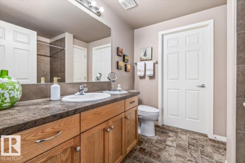 Bathroom featuring a double vanity with wood cabinetry, a large mirror, and textured flooring - 332 612 111 Street, Edmonton, AB - Indoor Photo Showing Bathroom