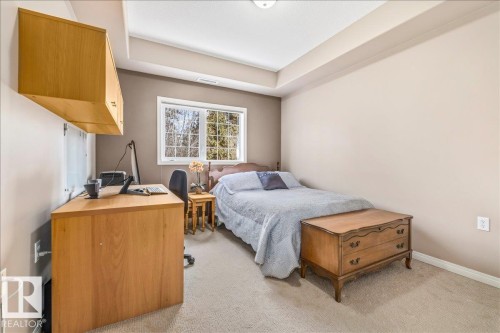 Well-proportioned room featuring a window with a view of mature trees, tray ceiling, and neutral carpet flooring - 332 612 111 Street, Edmonton, AB - Indoor Photo Showing Bedroom