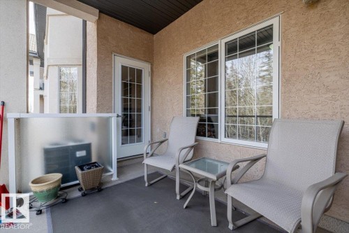 The property features a private balcony with a textured wall, a glass-paneled door, and windows providing views of exterior trees - 332 612 111 Street, Edmonton, AB - Outdoor With Deck Patio Veranda With Exterior