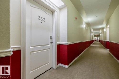 The property features a white paneled entry door with visible numbering and hardware, set within a well-lit interior hallway - 332 612 111 Street, Edmonton, AB - Indoor Photo Showing Other Room