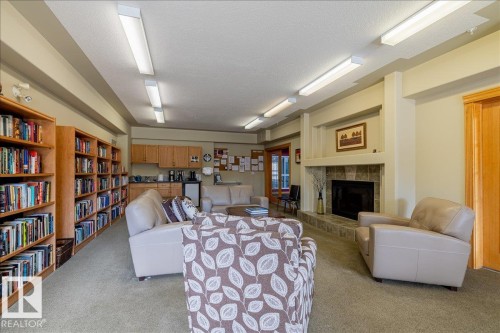 Community lounge area with ample seating, a stone-faced fireplace, and built-in bookshelves - 332 612 111 Street, Edmonton, AB - Indoor