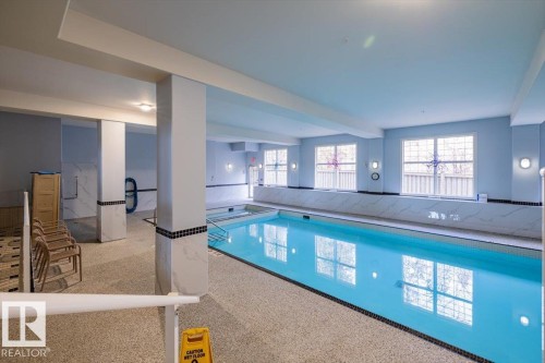 Indoor swimming pool featuring a light blue tiled pool, large windows, and wall-mounted lighting fixtures - 332 612 111 Street, Edmonton, AB - Indoor Photo Showing Other Room With In Ground Pool