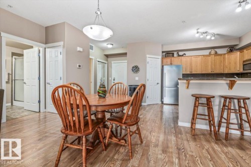 This open-concept area features wood-look flooring and includes a dining area with an overhead light fixture - 332 612 111 Street, Edmonton, AB - Indoor Photo Showing Dining Room