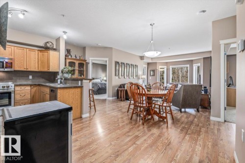 Open concept living area featuring wood flooring, a kitchen with wood cabinetry and stainless steel appliances, a dining area with a chandelier, and a living room with large windows - 332 612 111 Street, Edmonton, AB - Indoor