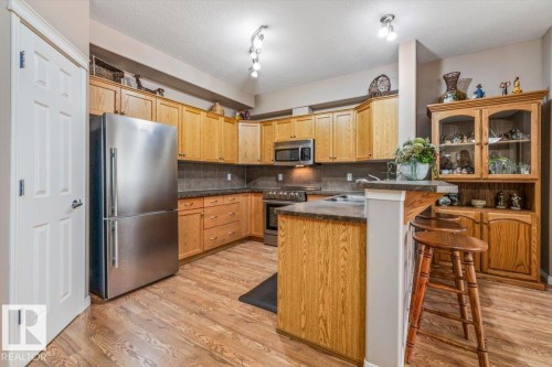 The kitchen features wood cabinetry, stainless steel appliances, and a breakfast bar with seating - 332 612 111 Street, Edmonton, AB - Indoor Photo Showing Kitchen