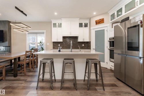 Open concept kitchen featuring an island with a light-colored countertop, white cabinetry with glass-fronted upper cabinets, and stainless steel appliances - 6193 Carr Road, Edmonton, AB - Indoor