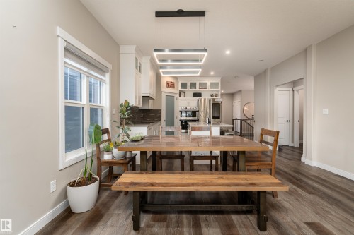 The open concept living area features resilient plank flooring, a modern linear chandelier, and a bright window providing natural light - 6193 Carr Road, Edmonton, AB - Indoor Photo Showing Dining Room