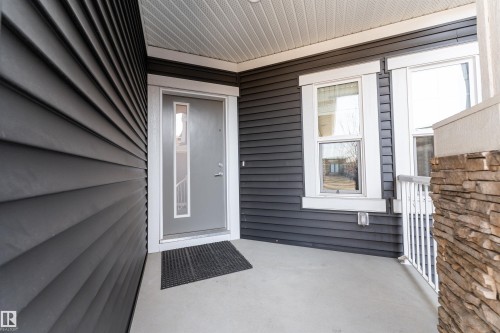 The property features dark gray horizontal siding, a light gray entry door with decorative glass, white window trim, and a stone accent column on the porch - 6193 Carr Road, Edmonton, AB - Outdoor With Exterior