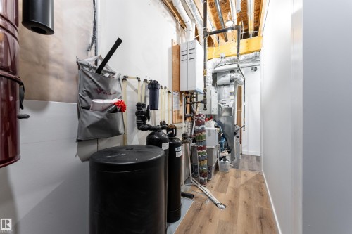 The utility area features exposed ceiling joists and various systems, including a water softener and tankless  water heater - 6193 Carr Road, Edmonton, AB - Indoor