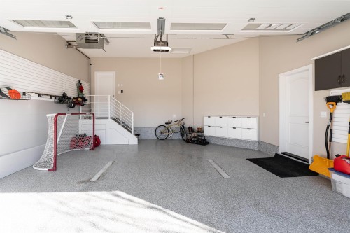 The property offers a spacious garage featuring a durable speckled epoxy floor coating, built-in storage cabinets, and a set of stairs with a white railing - 6193 Carr Road, Edmonton, AB - Indoor Photo Showing Garage