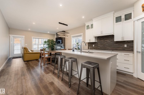 Open concept living space featuring hardwood floors, a kitchen island with seating, white cabinetry, and a dark tiled backsplash - 6193 Carr Road, Edmonton, AB - Indoor Photo Showing Kitchen With Upgraded Kitchen
