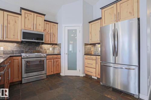 The kitchen features natural wood cabinetry, stainless steel appliances, a tiled backsplash, and dark floor tiles - 205 79 Street Sw, Edmonton, AB - Indoor Photo Showing Kitchen