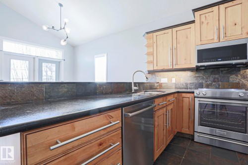 The kitchen features dark countertops, natural wood cabinetry, and stainless steel appliances including a range, microwave, and dishwasher - 205 79 Street Sw, Edmonton, AB - Indoor Photo Showing Kitchen